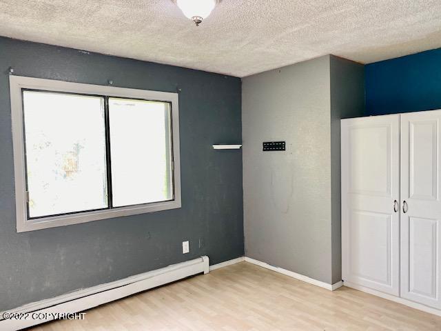 unfurnished bedroom featuring baseboard heating, a closet, a textured ceiling, and light wood-type flooring