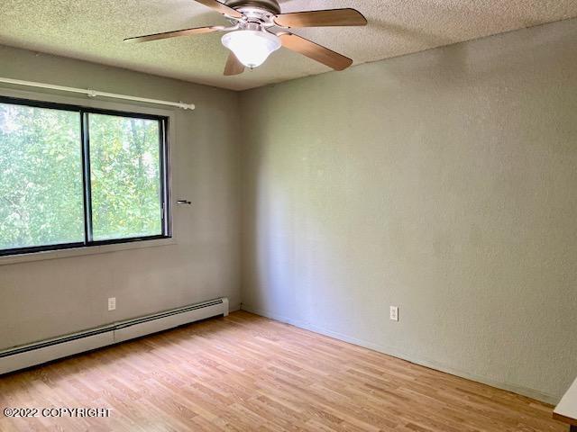 empty room with ceiling fan, light wood-type flooring, a textured ceiling, and a baseboard radiator