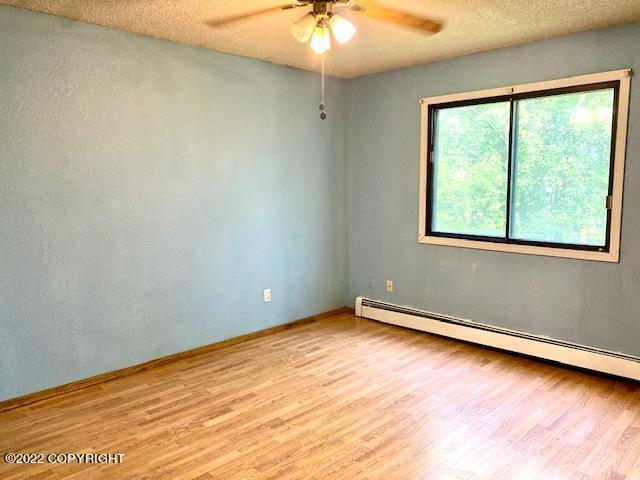 unfurnished room featuring baseboard heating, ceiling fan, a textured ceiling, and light wood-type flooring