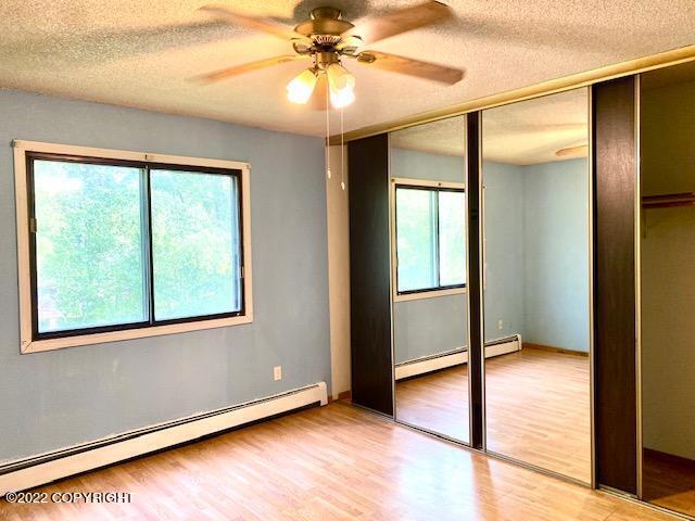 unfurnished bedroom featuring baseboard heating, ceiling fan, and light hardwood / wood-style floors