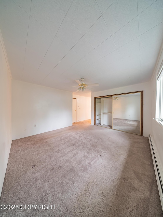 carpeted spare room featuring ceiling fan, built in features, and a baseboard heating unit