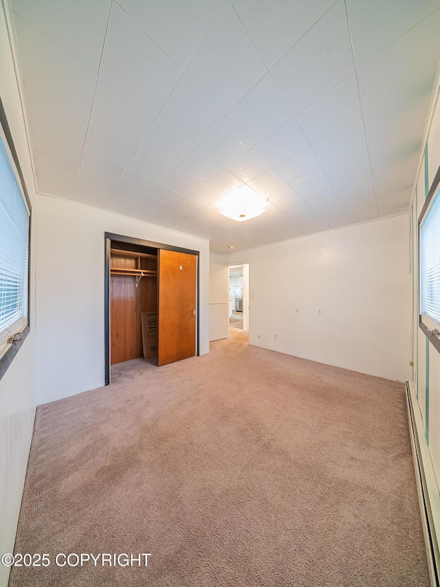 unfurnished bedroom with carpet flooring, a closet, and a baseboard radiator