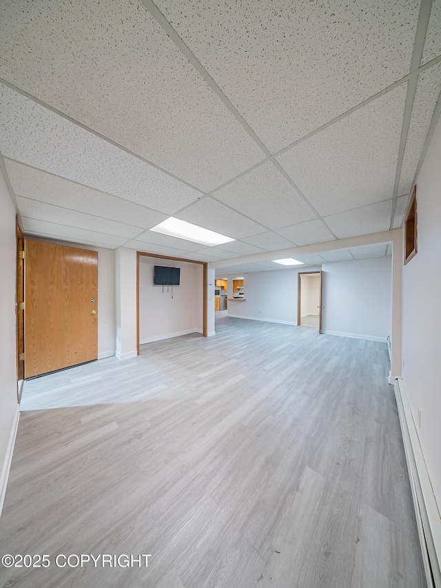 basement with a paneled ceiling, a baseboard radiator, and light wood-type flooring