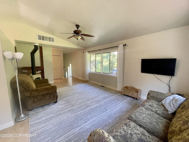 living room with ceiling fan, vaulted ceiling, hardwood / wood-style floors, and a wood stove