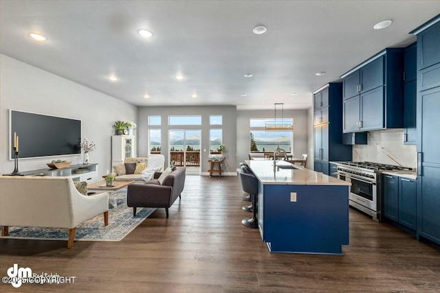 kitchen featuring high end stainless steel range oven, a center island with sink, blue cabinets, hanging light fixtures, and sink