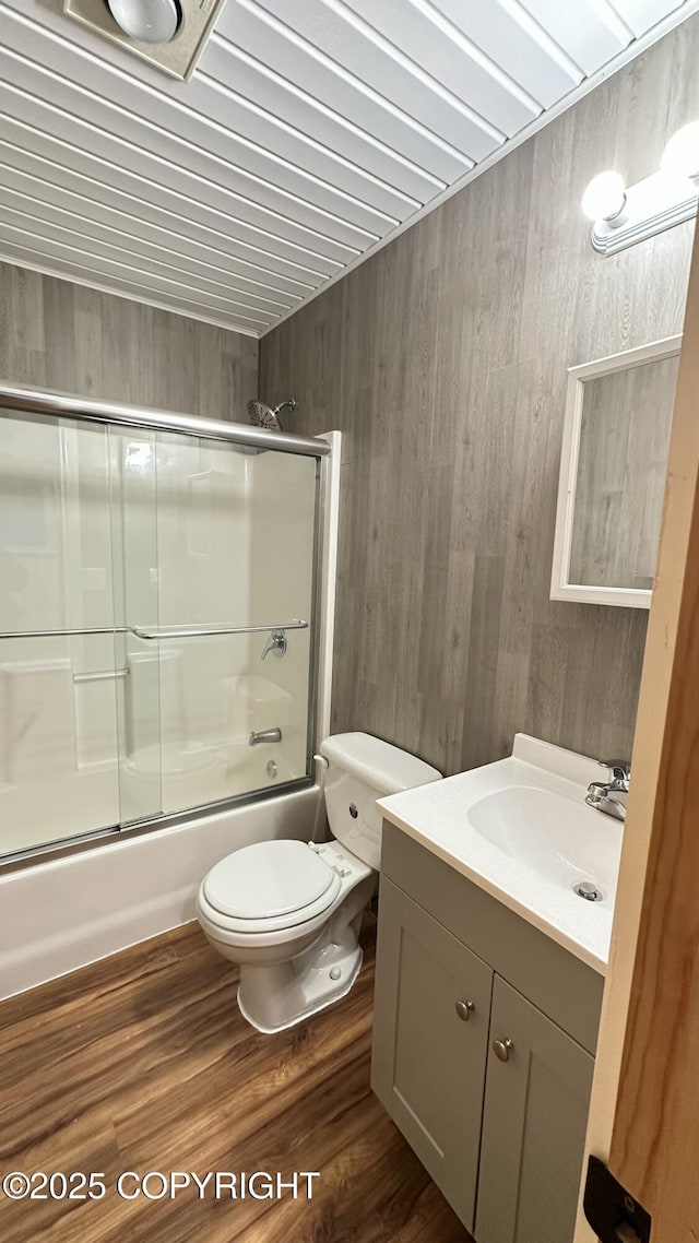 full bathroom featuring toilet, vanity, wooden walls, hardwood / wood-style flooring, and enclosed tub / shower combo