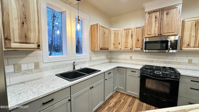 kitchen featuring gas stove, backsplash, decorative light fixtures, light stone counters, and sink