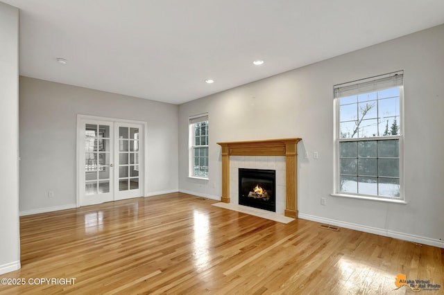 unfurnished living room featuring french doors, a tile fireplace, and light hardwood / wood-style floors