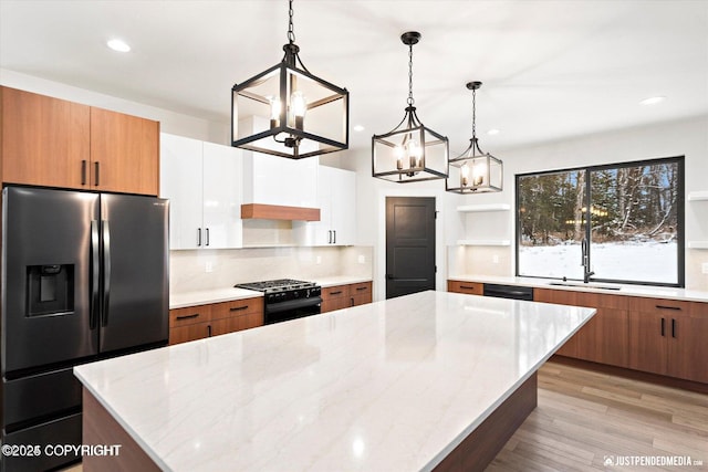 kitchen with decorative light fixtures, a kitchen island, black appliances, white cabinetry, and light stone countertops