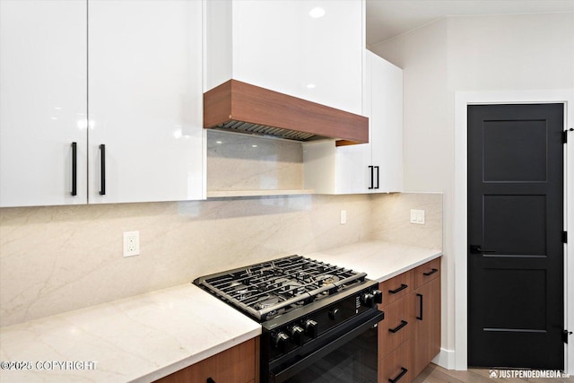 kitchen with custom range hood, white cabinets, tasteful backsplash, and black range with gas cooktop