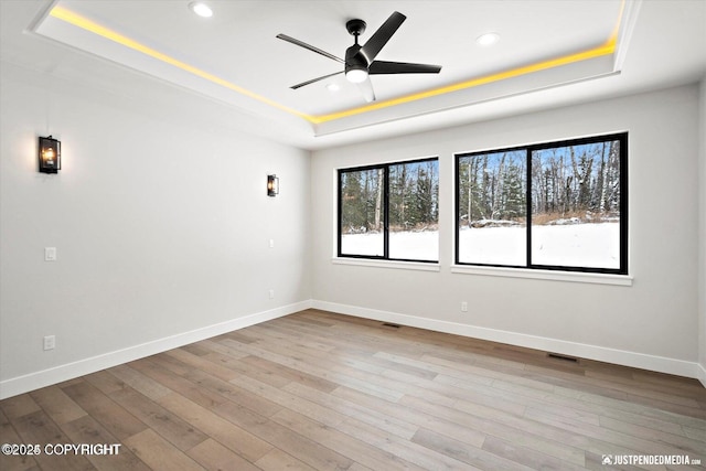 unfurnished room featuring ceiling fan, light hardwood / wood-style flooring, and a raised ceiling