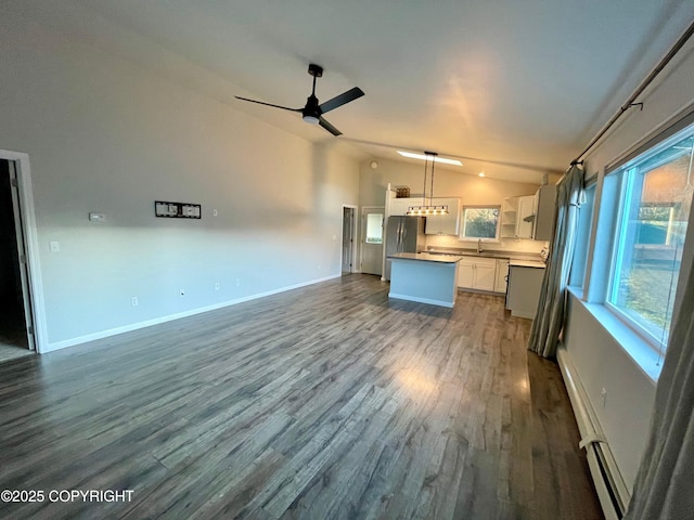 kitchen featuring lofted ceiling, stainless steel fridge, white cabinets, hanging light fixtures, and baseboard heating