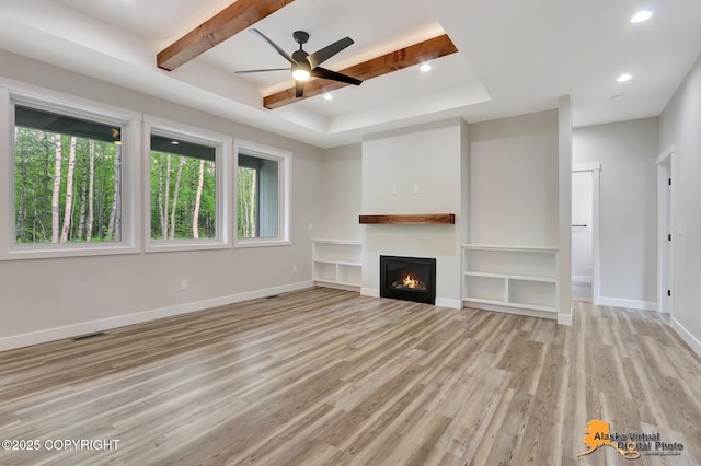 unfurnished living room with light wood-type flooring, ceiling fan, and a raised ceiling