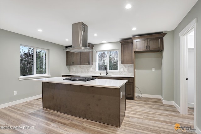 kitchen with island exhaust hood, tasteful backsplash, sink, stainless steel gas cooktop, and light hardwood / wood-style flooring