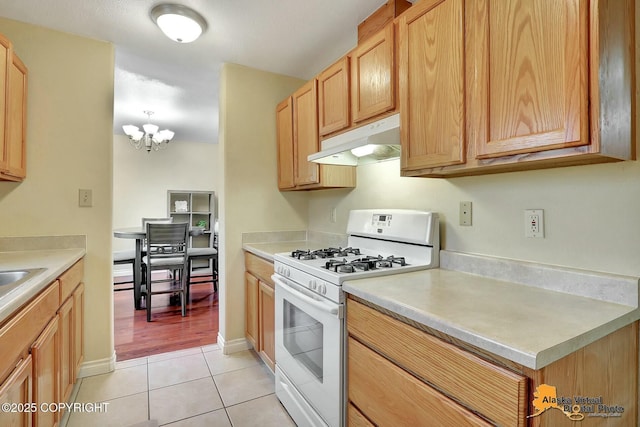 kitchen with light tile patterned flooring, light countertops, under cabinet range hood, a notable chandelier, and white gas range