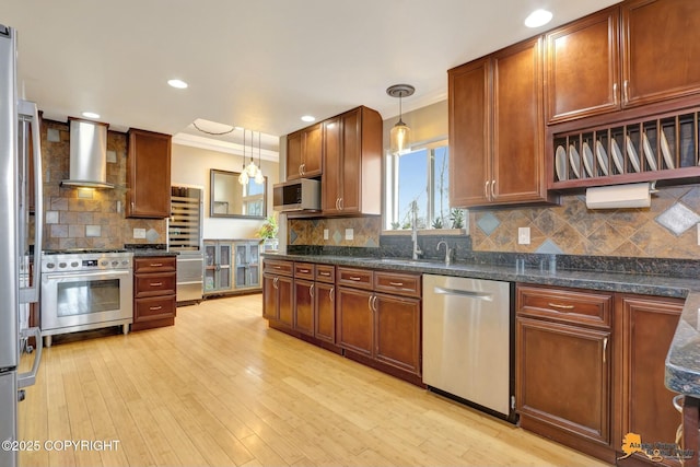 kitchen featuring stainless steel appliances, light wood-style floors, hanging light fixtures, and wall chimney exhaust hood