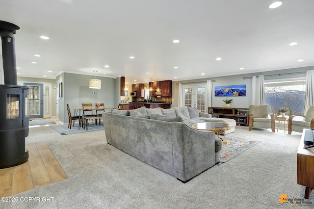 living room with crown molding, recessed lighting, light colored carpet, a wood stove, and baseboards