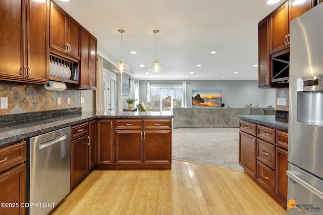 kitchen featuring light wood finished floors, decorative backsplash, open floor plan, a peninsula, and stainless steel appliances