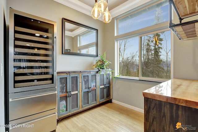 interior space featuring light wood-style flooring, ornamental molding, beverage cooler, and baseboards