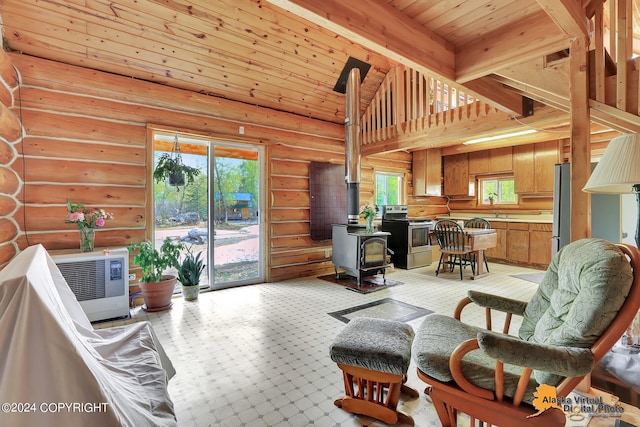 living room featuring a towering ceiling, rustic walls, a wood stove, and a healthy amount of sunlight