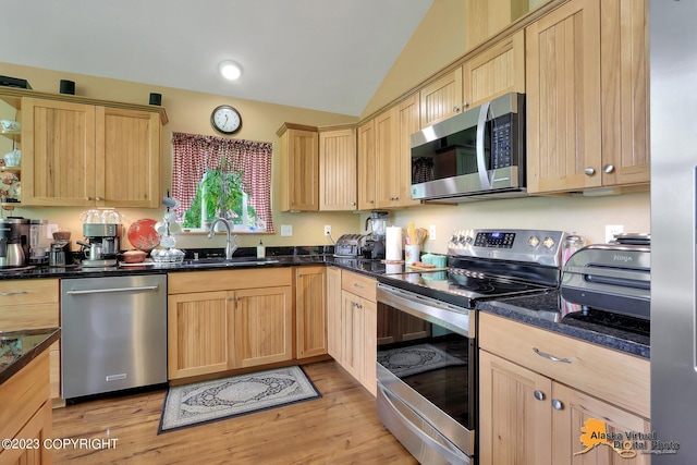 kitchen with stainless steel appliances, sink, vaulted ceiling, and dark stone counters