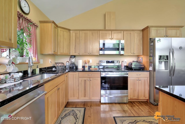 kitchen featuring sink, vaulted ceiling, dark stone countertops, light hardwood / wood-style floors, and appliances with stainless steel finishes