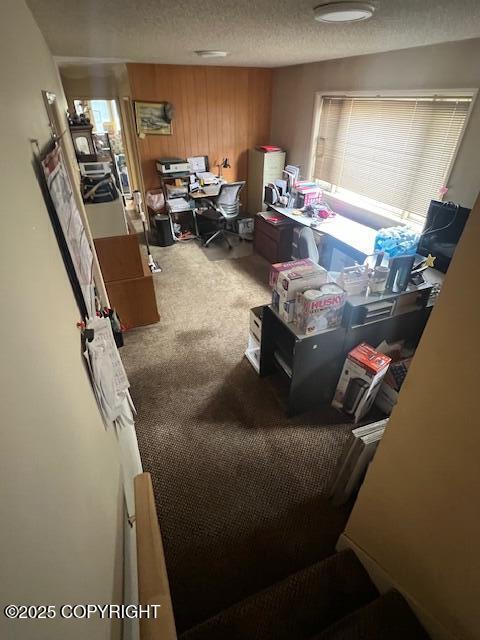 carpeted home office with wood walls and a textured ceiling