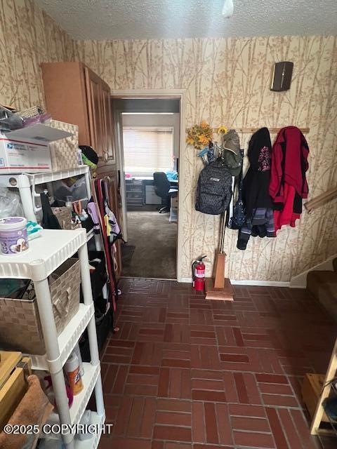 mudroom with brick floor, wallpapered walls, and a textured ceiling