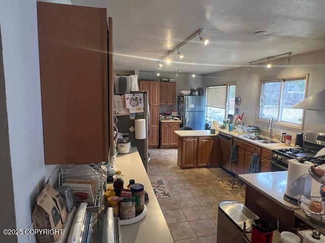 kitchen featuring appliances with stainless steel finishes, a sink, light countertops, rail lighting, and brown cabinetry