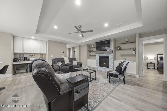 living room featuring light hardwood / wood-style floors, built in shelves, a tray ceiling, and a fireplace