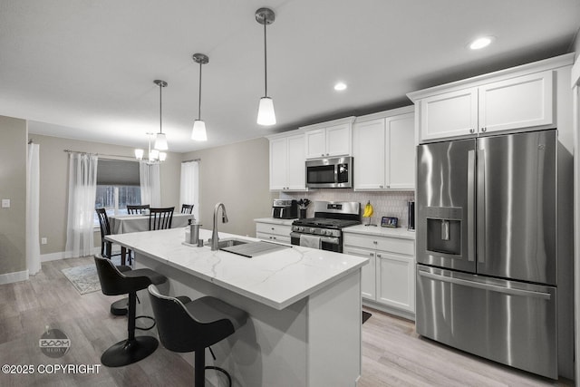 kitchen with light stone countertops, appliances with stainless steel finishes, a kitchen island with sink, white cabinets, and pendant lighting