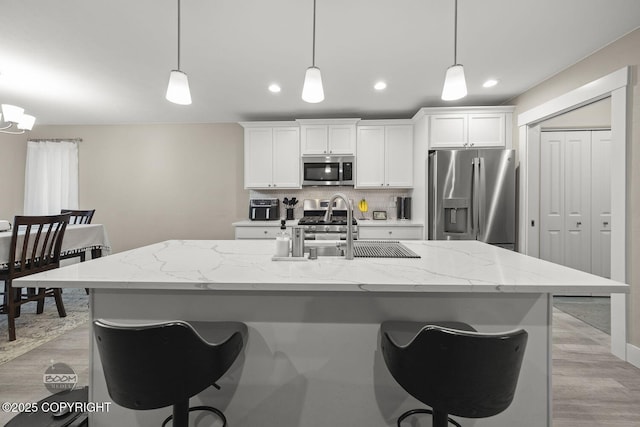 kitchen with stainless steel appliances, white cabinetry, a kitchen island with sink, and pendant lighting