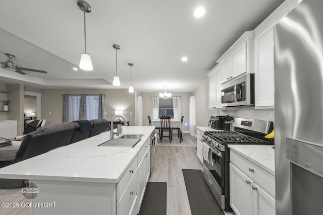 kitchen with appliances with stainless steel finishes, sink, decorative light fixtures, white cabinets, and a center island with sink