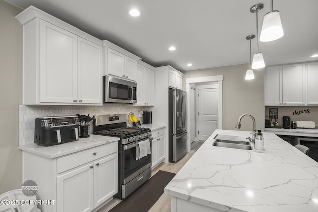 kitchen featuring white cabinetry, stainless steel appliances, sink, hanging light fixtures, and light stone counters