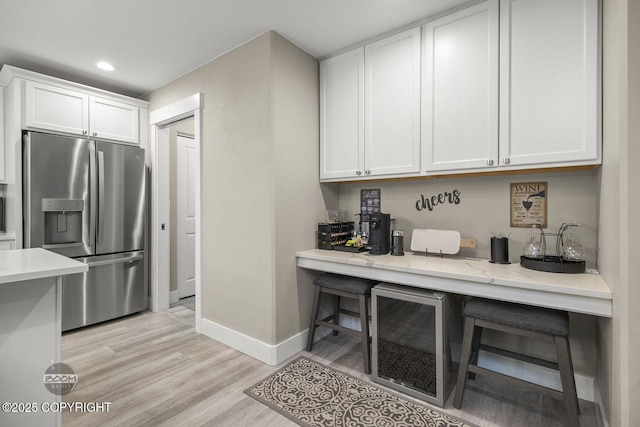 kitchen with white cabinets, light stone counters, light hardwood / wood-style floors, and stainless steel fridge