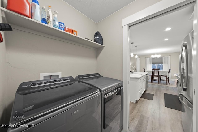 laundry area with light hardwood / wood-style flooring, sink, washer and dryer, a textured ceiling, and a notable chandelier