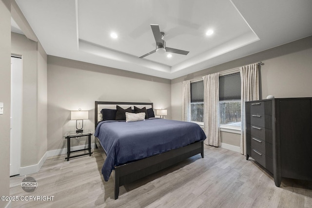 bedroom with light wood-type flooring, ceiling fan, and a tray ceiling