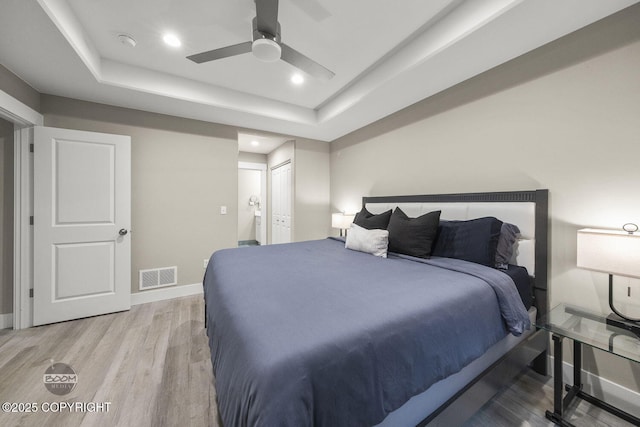 bedroom with light wood-type flooring, ceiling fan, a closet, and a tray ceiling