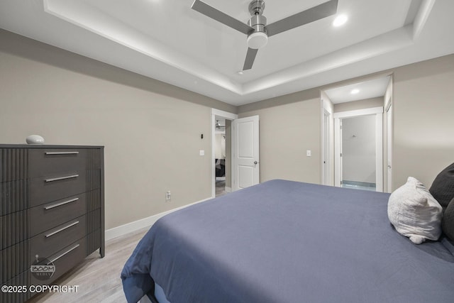 bedroom featuring ceiling fan, light hardwood / wood-style floors, and a tray ceiling