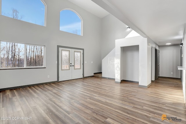 unfurnished living room with french doors, a high ceiling, and light wood-type flooring