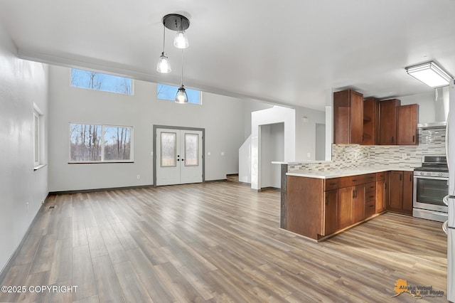 kitchen featuring hanging light fixtures, light wood-type flooring, kitchen peninsula, stainless steel stove, and decorative backsplash