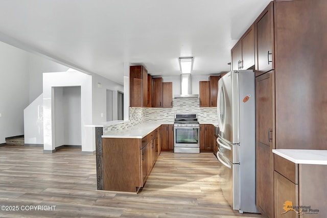 kitchen with tasteful backsplash, stainless steel appliances, light hardwood / wood-style floors, and wall chimney exhaust hood