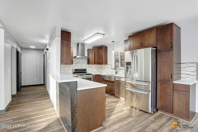 kitchen with pendant lighting, wall chimney range hood, sink, stainless steel appliances, and kitchen peninsula