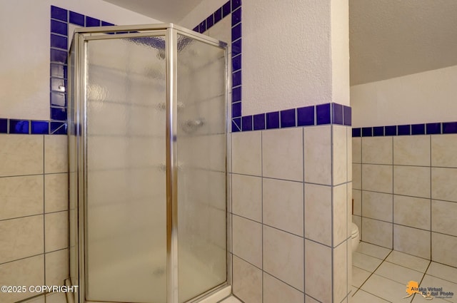 bathroom with an enclosed shower, tile patterned flooring, tile walls, and toilet