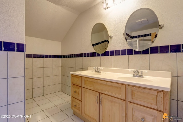 bathroom featuring tile patterned floors, vaulted ceiling, a textured ceiling, tile walls, and vanity