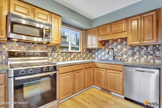 kitchen with stainless steel appliances, sink, light wood-type flooring, and decorative backsplash