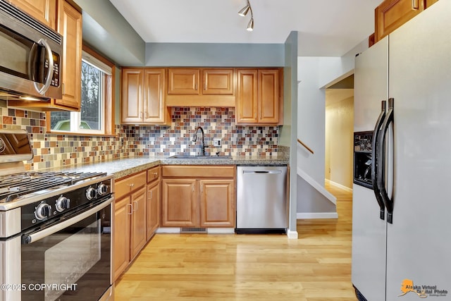 kitchen with appliances with stainless steel finishes, sink, decorative backsplash, and light hardwood / wood-style flooring