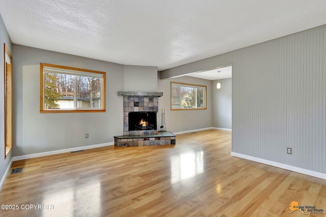 unfurnished living room featuring a wealth of natural light, a textured ceiling, a stone fireplace, and light wood-type flooring