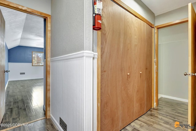 hallway with vaulted ceiling, light hardwood / wood-style floors, and a textured ceiling