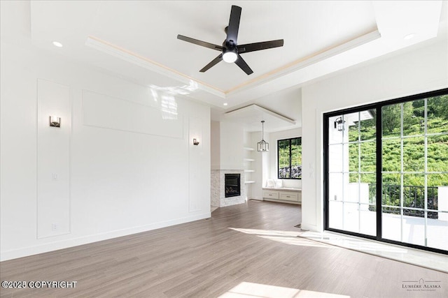 1690 W Valley Ridge Dr, Wasilla, AK 99654 - unfurnished living room featuring a raised ceiling, a glass covered fireplace, ornamental molding, wood finished floors, and a ceiling fan